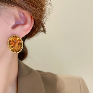 Close-up of amber resin irregular oval earrings with twisted gold metal trim on model