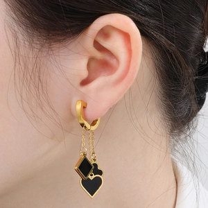 Close-up of gold tassel earrings with black heart and flower charms on female model