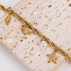 Gold ocean themed bracelet with seashell, starfish, and pearl charms on stone surface