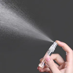 Portable clear glass perfume spray bottle dispensing a fine mist shown in use
