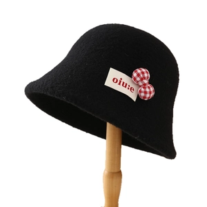 Black lamb wool bucket hat with cute plaid bow and side label on a wooden stand