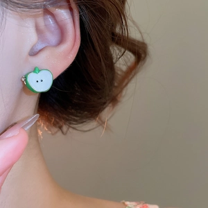 Close-up of model wearing green and white apple-shaped enamel C-style earrings