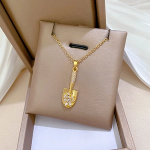 Detailed macro view of a gold shovel pendant necklace with sparkling crystal inlay inside a box