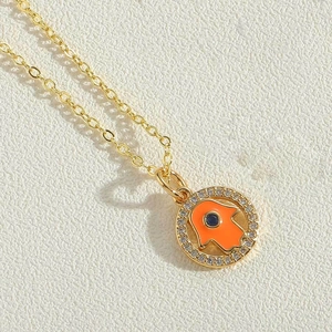 Close-up of golden Hamsa Hand pendant with orange enamel and blue stone detail