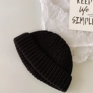Vista detallada del gorro de punto negro con textura tejida en un escritorio blanco