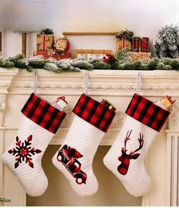 Dreiteiliges Set weißer Weihnachtsstrümpfe mit rot-schwarzem Karomuster hängend am Kamin