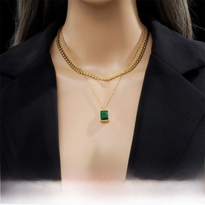 Detail of layered gold necklace with emerald rectangle stone pendant on model