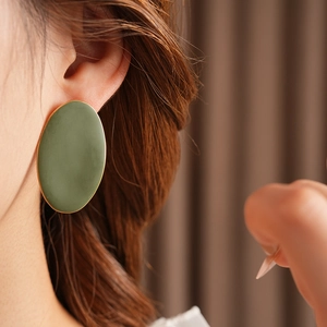 Dettaglio di un grande orecchino ovale verde con bordo dorato indossato da una modella