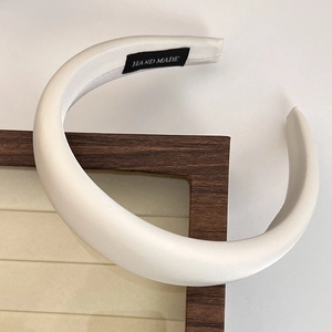 Close-up of white padded satin headband with handmade label on beige jewelry tray