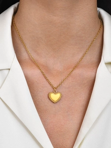 Close-up of a gold heart locket necklace with beaded edges worn on a white shirt