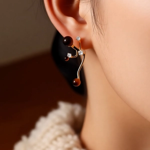 Detail of golden irregular earrings with dark tiger eye stones and zircons on a model