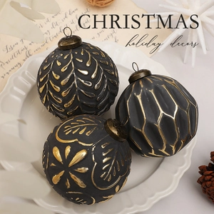 Detail of matte black and gold 8cm Christmas balls with relief patterns on a white plate