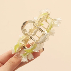 Detail of a golden lily of the valley hair claw clip with white flowers and green leaves