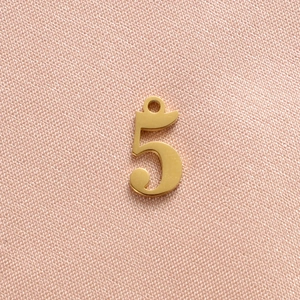 Macro view of gold-plated number five pendant with integrated hanging loop and matte finish