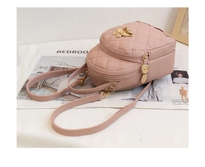 Detailed view of pink quilted mini backpack with golden zippers and cat charm