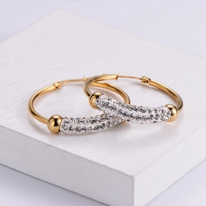 Golden hoop earrings with zircon pavé accents on white pedestal for modern ear styling