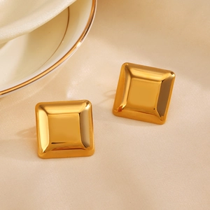 Polished gold square stainless steel stud earrings on beige silk background fabric
