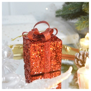 Detail of red glitter gift box ornament with bow on reflective surface and festive decor