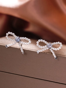 Macro detail of bow-shaped pearl earrings with a central cubic zirconia stone
