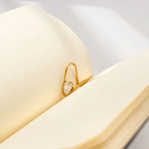 Macro shot of minimalist gold ear cuff with pear-cut zircon clipped on book pages