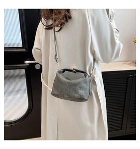 Detail of grey vintage leather crossbody bag with metal buckle on a model wearing a coat