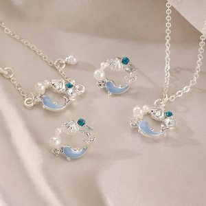 Detailed shot of blue dolphin necklace and pearl earrings set on elegant silk fabric