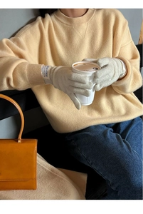 Detail of beige wool knitted gloves featuring ribbed cuffs and branded textile labels