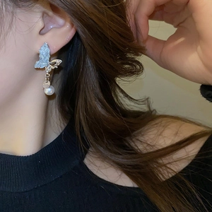 Détail d'une boucle d'oreille papillon asymétrique avec texture bleu clair et perle sur modèle