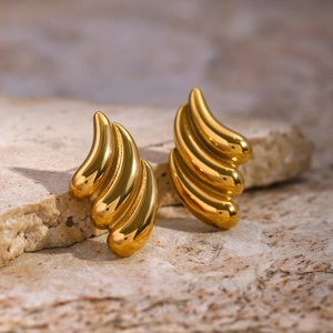 Macro shot of gold-plated wing earrings on natural stone showing metallic texture