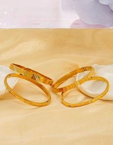 Detail of four-piece 18k gold plated stainless steel bangles with crystal clover and Greek key patterns