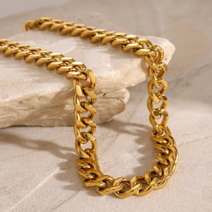 Close-up of golden Cuban link necklace made of stainless steel on natural beige stone