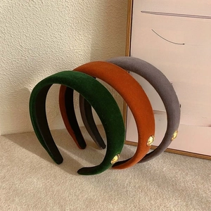 Three velvet headbands in green, orange, and gray with golden decorative metal tags