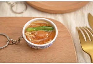 Macro shot of miniature PVC food keychain with noodles and blue floral patterned bowl