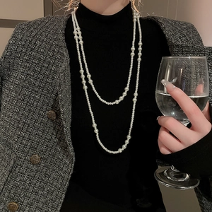 Elegant multi-layer long pearl necklace over black sweater and tweed coat