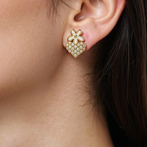 Close-up of model wearing gold heart and white flower clover stud earrings with white zircons