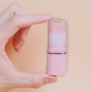 Hand holding a portable pink mini makeup brush with a clear dust lid for easy travel