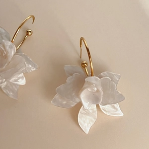 Vue macro de boucles d'oreilles fleurs 3D en résine blanche avec pétales nacrés et crochets