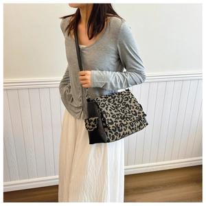 Detail of leopard print canvas tote bag featuring black leather straps and side pocket