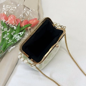 Detail view of the open white shell bag with green floral pattern and pearl handle