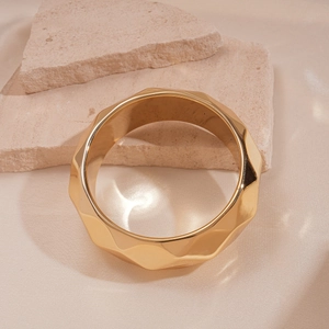 Macro detail of geometric faceted wide gold bracelet on natural stone and silk background