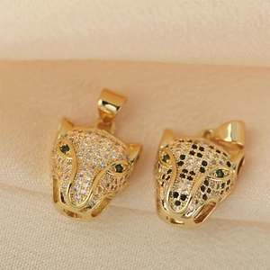 Golden leopard head pendants with zircon inlay and green gem eyes on beige fabric background