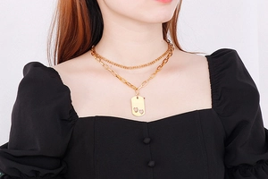Detail of a double-layered gold necklace with square pendant and hollow hearts on model