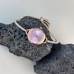 Macro detail of rose gold bracelet watch with pink sunray dial on a volcanic stone