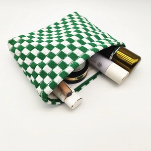 Macro detail of spacious green and white checkered knit pouch filled with cosmetics