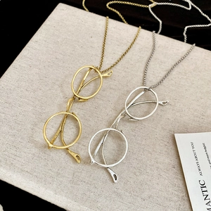 Detail of eye-frame pendant necklaces in gold and silver finish on linen texture