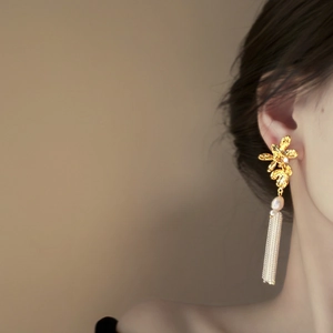 Boucles d'oreilles fleurs dorées avec perle et longs pompons métalliques sur modèle