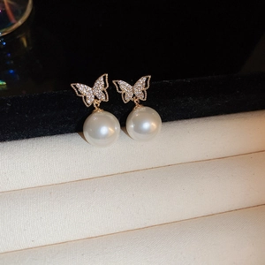 Macro detail of golden butterfly stud earrings featuring micro-pave zircons and white pearls