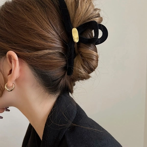 Détail d'une pince à cheveux en velours noir avec boucle dorée sur un chignon élégant