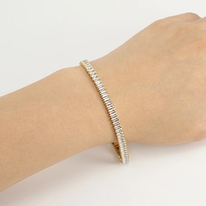 Detail of emerald-cut zircon tennis bracelet in gold finish worn on wrist