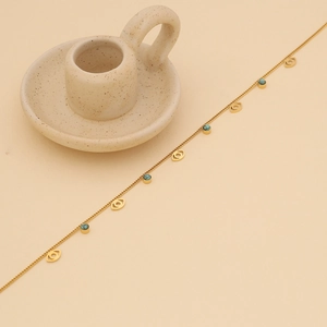 Close-up of golden chain necklace with turquoise beads and evil eye charm details